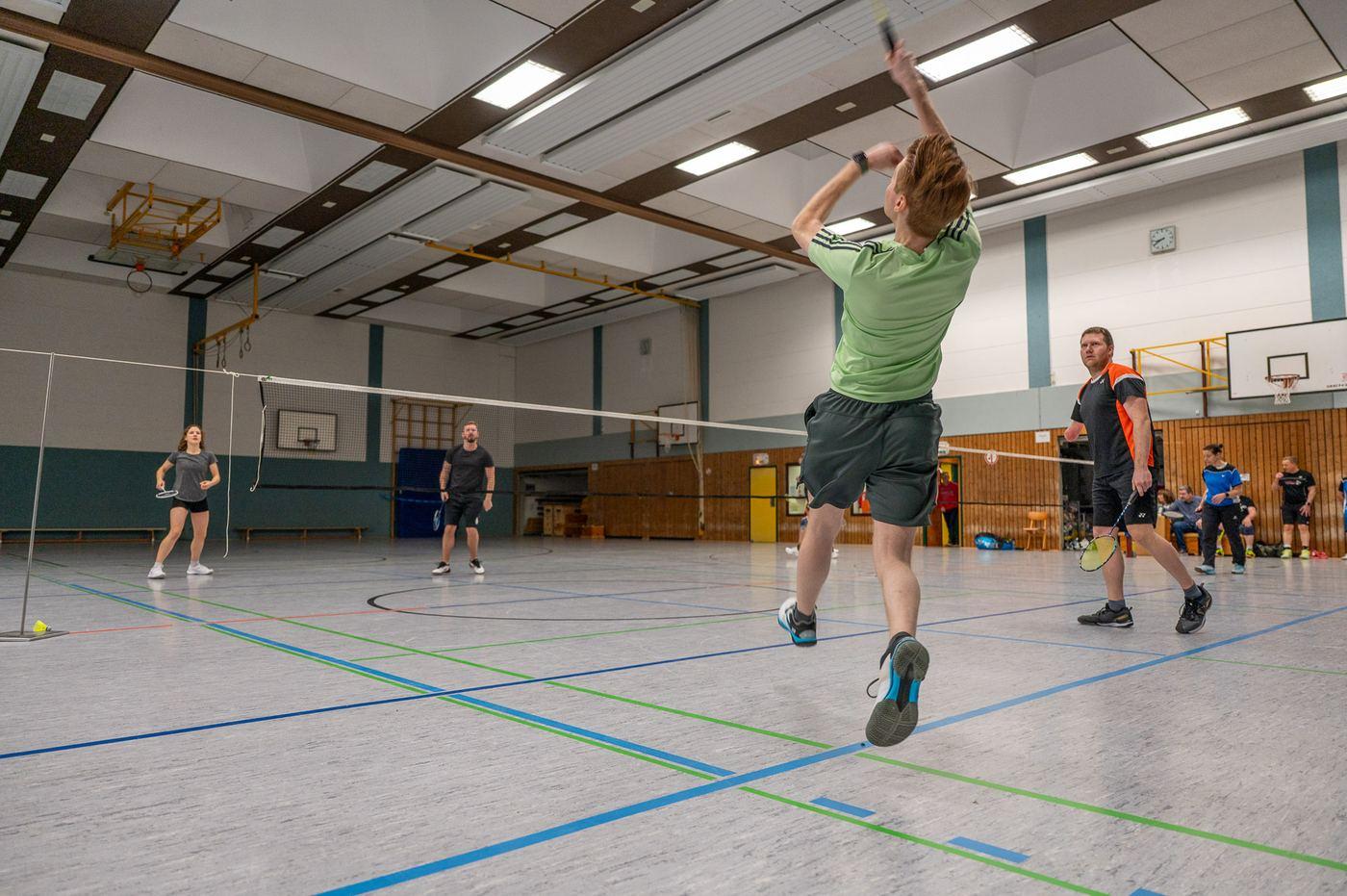 Blick über zwei nebeneinanderliegende Felder in der Halle; rechts springt ein Spieler im grünen Shirt hoch zum Schlag.