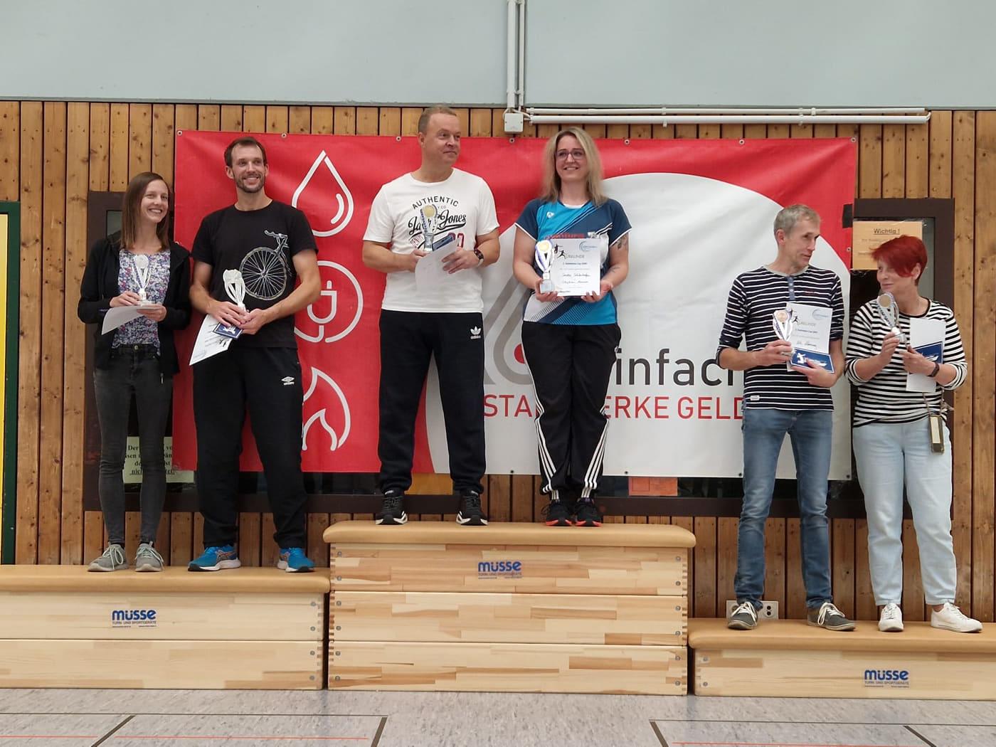 Sechs Spielerinnen und Spieler stehen bei der Siegerehrung im Mixed mit Pokalen und Urkunden auf dem Podest