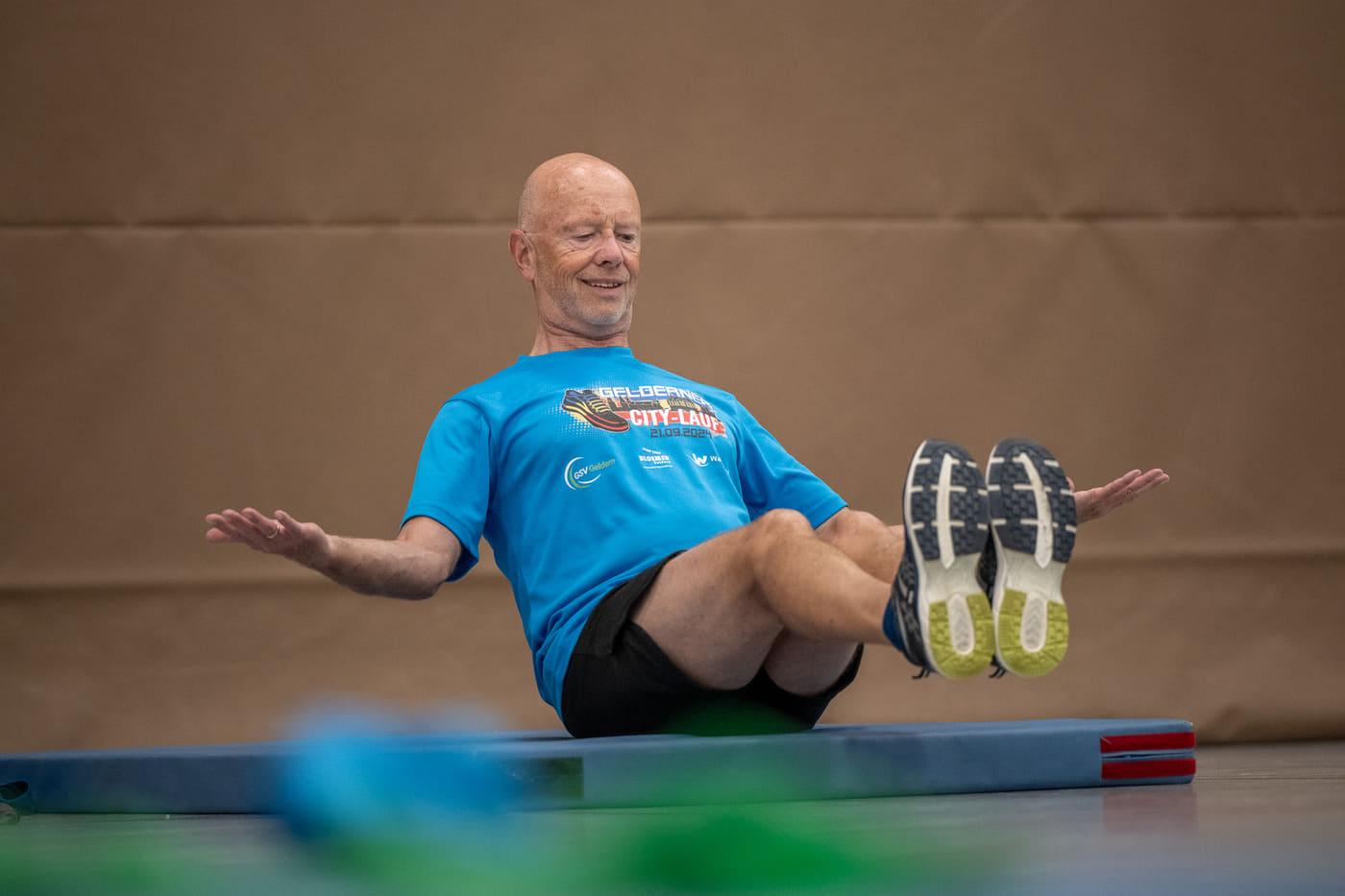 Ein Sportler im Citylauf-Shirt hält lächelnd die Bootshaltung auf der Matte
