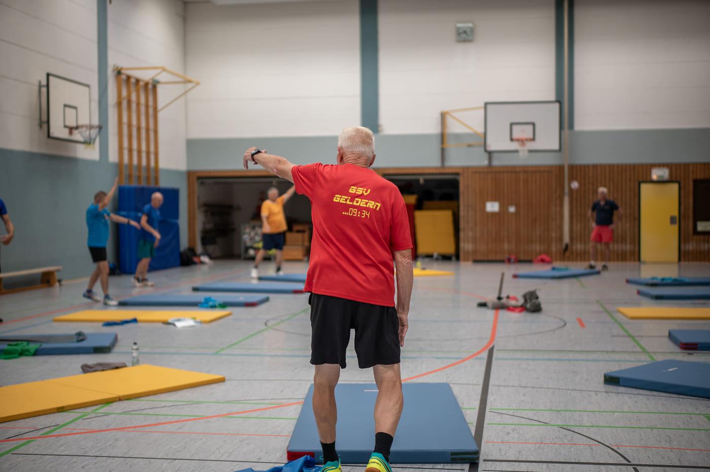 Der Übungsleiter im roten Vereinsshirt steht vor der Gruppe und stoppt die Zeit