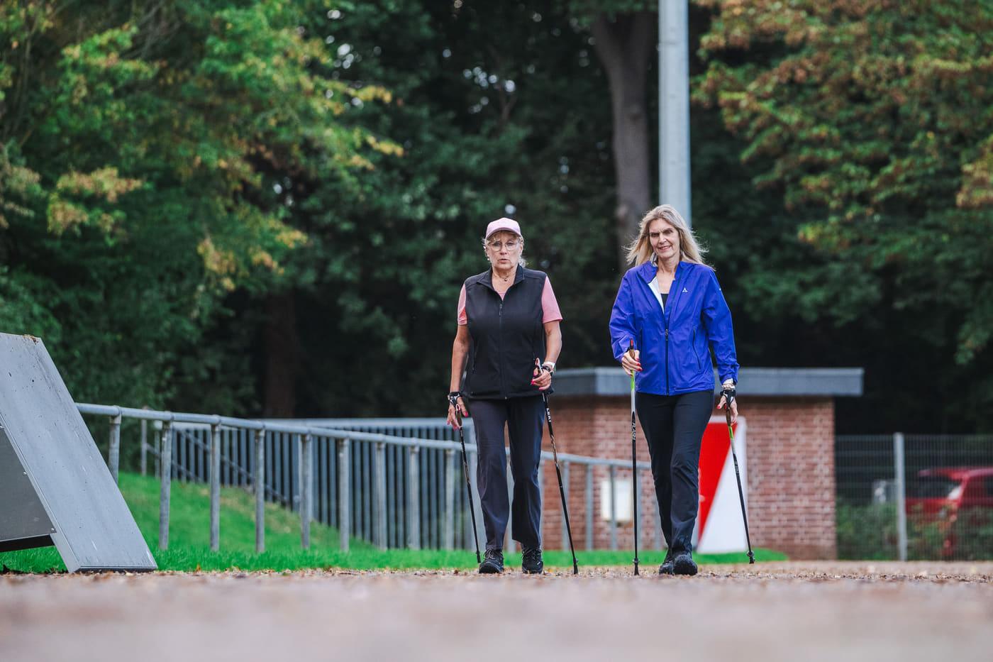 Zwei Walkerinnen setzen ihre Stöcke auf dem Weg neben dem Sportplatz auf