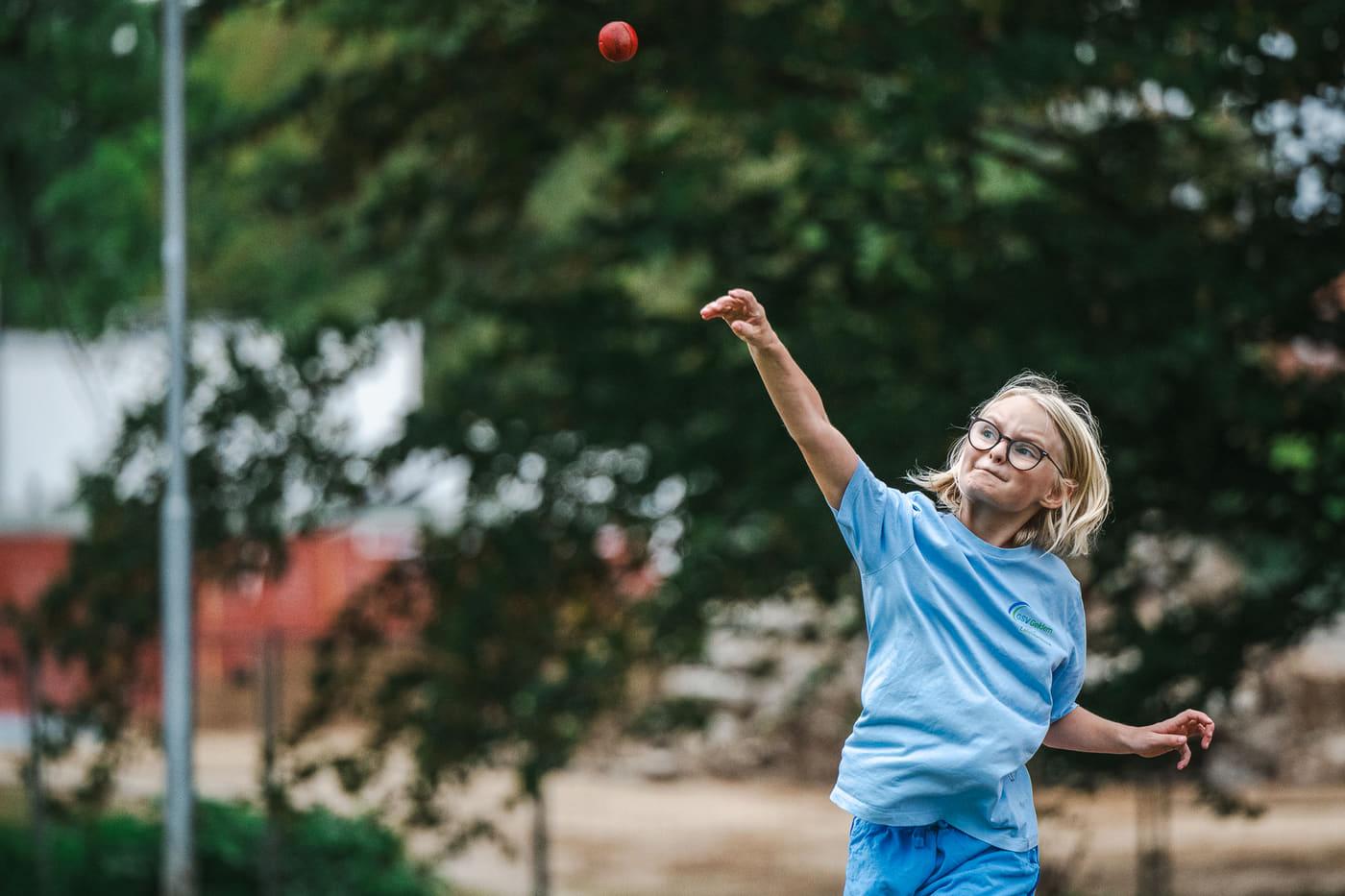 Mädchen mit Brille schaut dem gerade geworfenen roten Schlagball hinterher