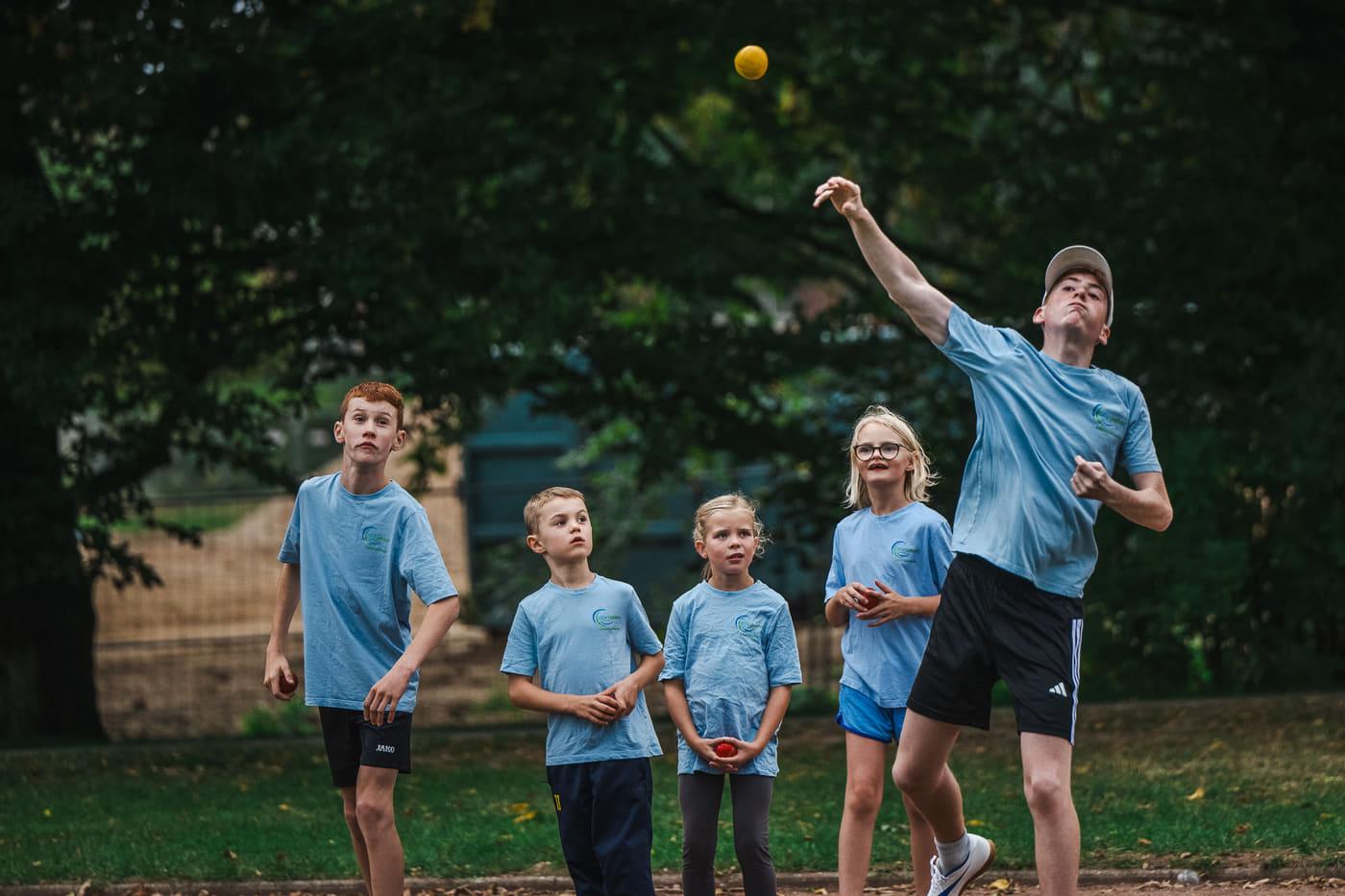 Wurf mit dem Schlagball, vier Kinder verfolgen den Flug mit den Augen