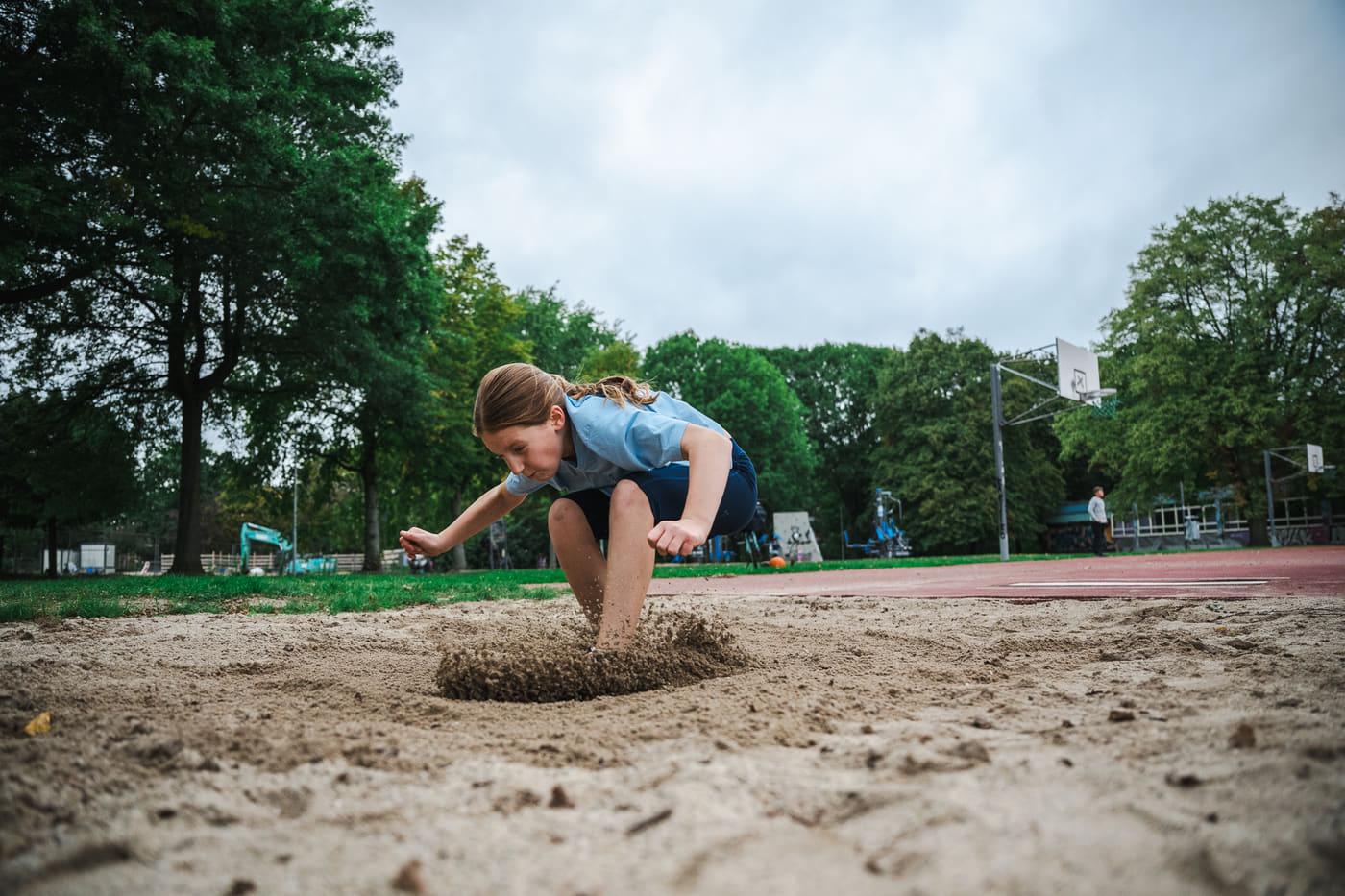 Mädchen landet im Sand, unter den Füßen spritzt eine Sandfontäne auf
