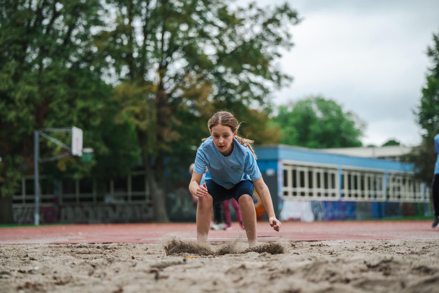 Mädchen fängt die Landung mit beiden Händen im Sand ab