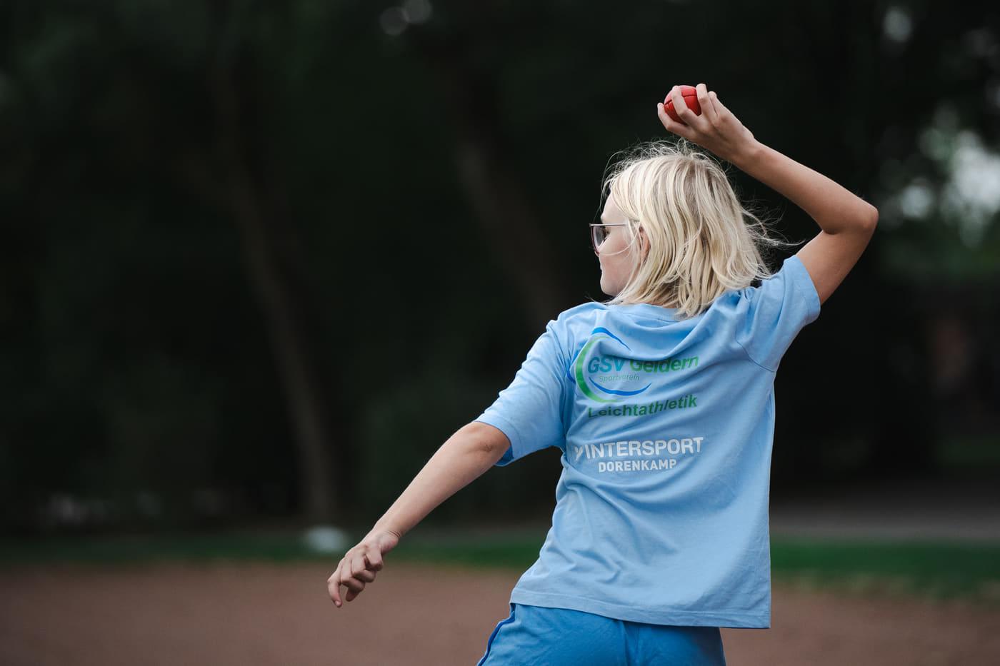 Mädchen holt mit dem Rücken zur Kamera zum Wurf aus, der Ball in der erhobenen Hand