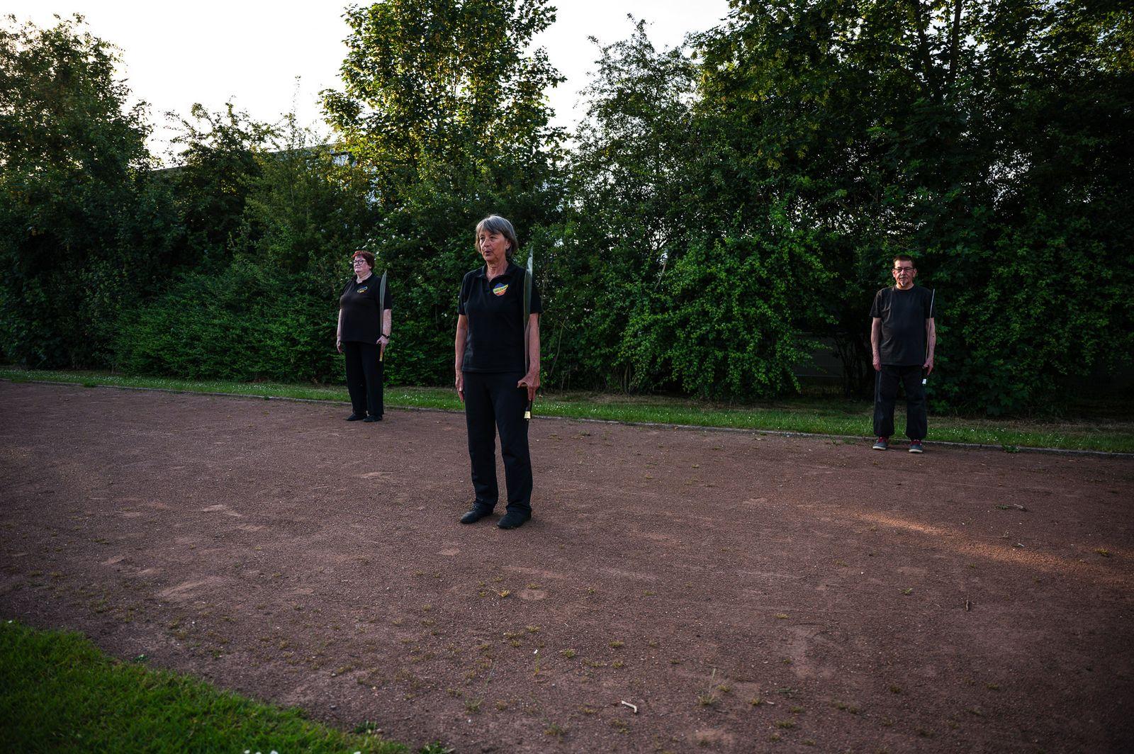 Einzelne Übende steht in Grundposition vor einer Hecke