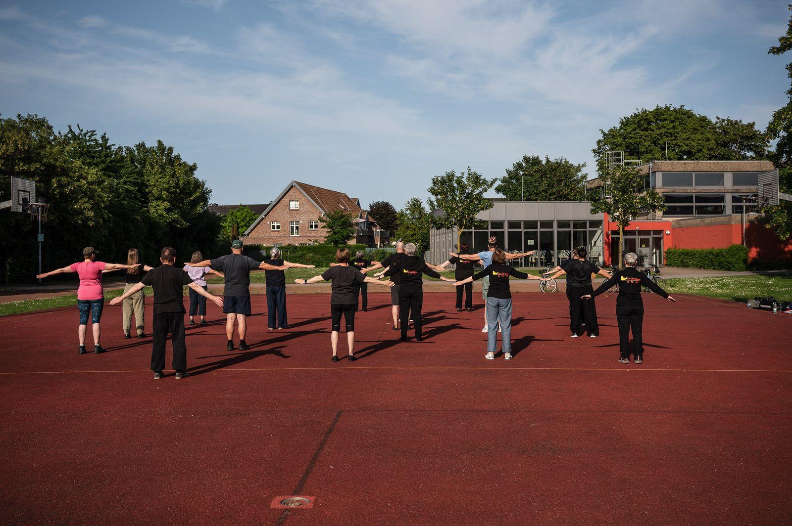 Die Tai-Chi-Gruppe übt in weitem Abstand eine Form auf dem Aschenplatz