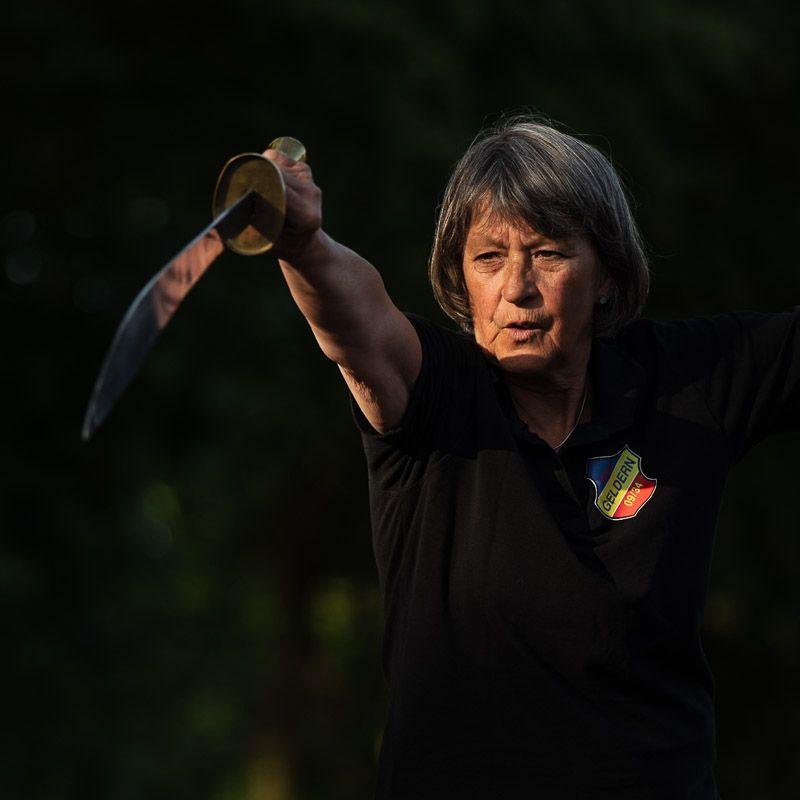 Übende streckt den Tai-Chi-Säbel in einer Form von sich, im Abendlicht vor dunklem Grün